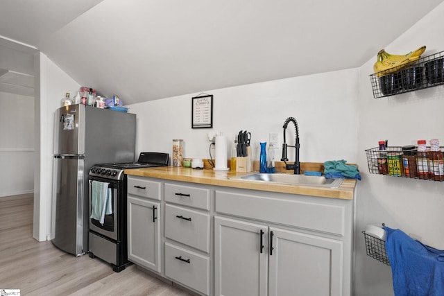 kitchen with lofted ceiling, light wood-style flooring, stainless steel appliances, wooden counters, and a sink