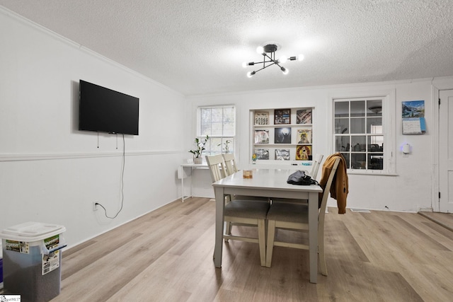 dining room with a textured ceiling, light wood finished floors, a notable chandelier, and crown molding