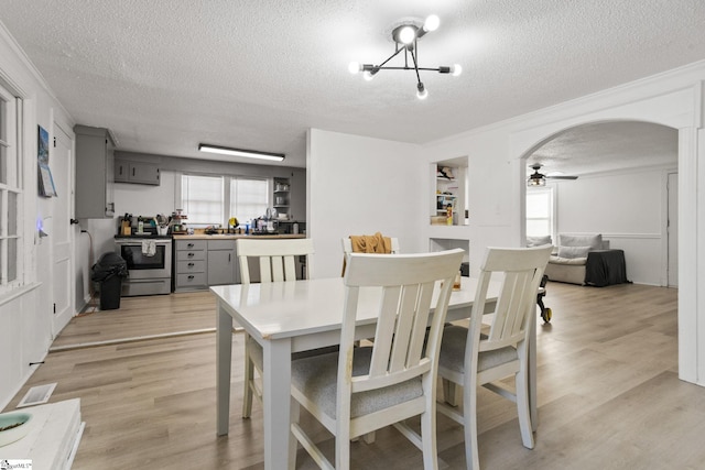 dining area with light wood-style floors, arched walkways, a textured ceiling, and a ceiling fan