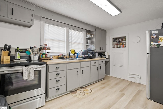 kitchen with open shelves, light countertops, appliances with stainless steel finishes, light wood-style floors, and a sink