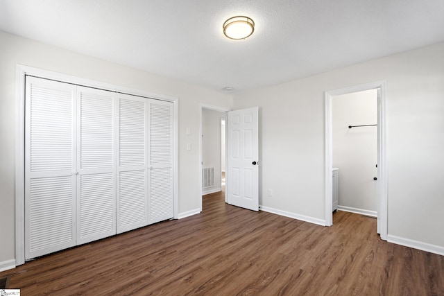 unfurnished bedroom with a closet, dark wood finished floors, visible vents, and baseboards