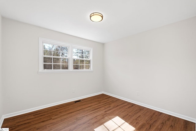 empty room featuring wood finished floors, visible vents, and baseboards