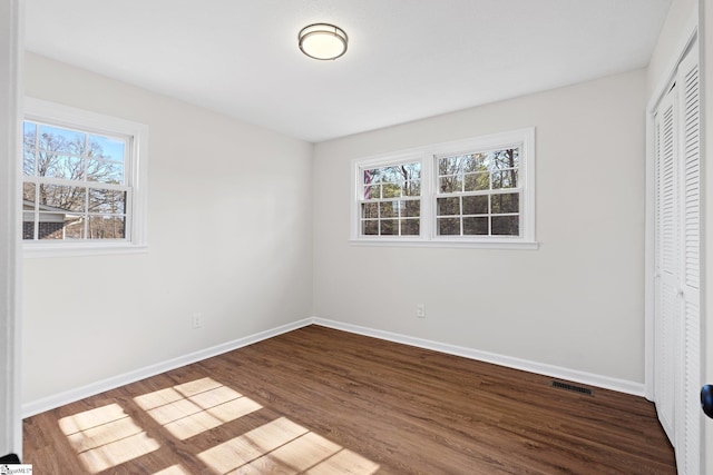 unfurnished bedroom with dark wood-style floors, multiple windows, baseboards, and a closet