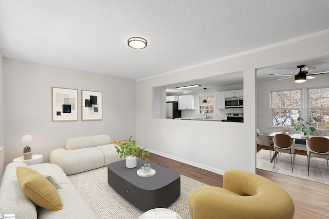 living room featuring light wood-style flooring, a ceiling fan, ornamental molding, a textured ceiling, and baseboards