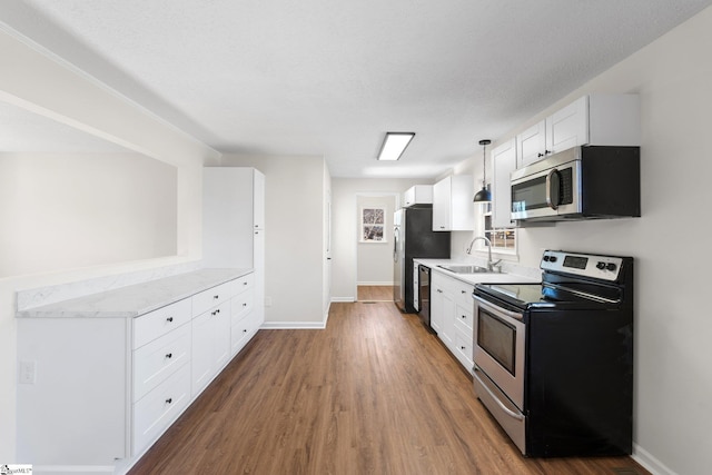 kitchen with appliances with stainless steel finishes, decorative light fixtures, light countertops, white cabinetry, and a sink