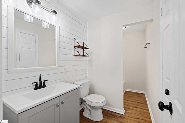 bathroom featuring toilet, wooden walls, wood finished floors, vanity, and baseboards