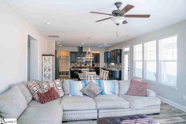 living room with visible vents, ceiling fan, baseboards, and wood finished floors