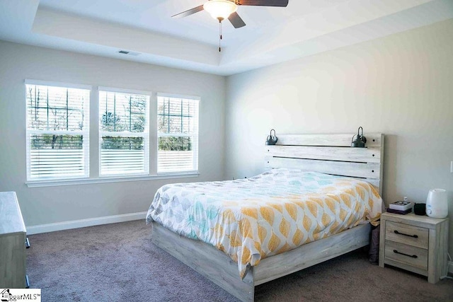 bedroom with a raised ceiling, visible vents, a ceiling fan, carpet flooring, and baseboards