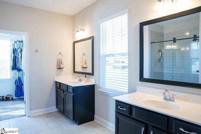 bathroom with a stall shower, a spacious closet, two vanities, and a sink