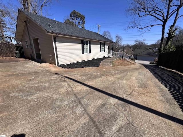 view of side of property with fence, an outdoor structure, and roof with shingles