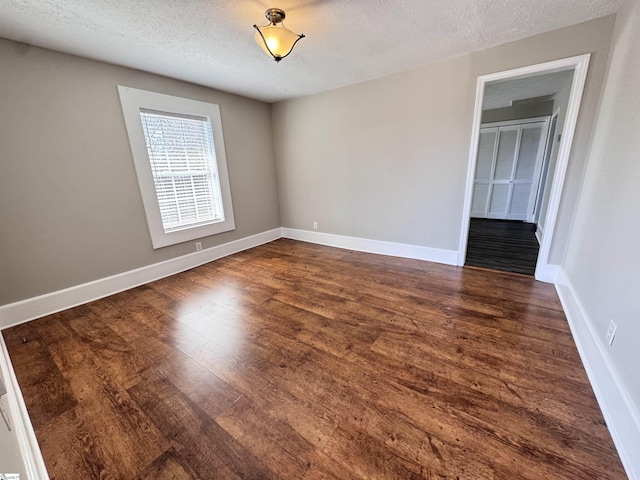 unfurnished room with a textured ceiling, baseboards, and dark wood-style flooring