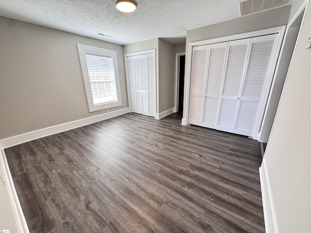 unfurnished bedroom featuring dark wood finished floors, two closets, visible vents, a textured ceiling, and baseboards