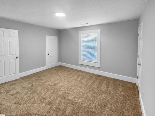 carpeted empty room with visible vents, a textured ceiling, and baseboards