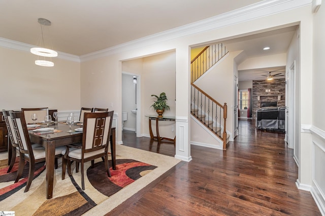 dining area featuring baseboards, stairway, ornamental molding, dark wood-type flooring, and a stone fireplace