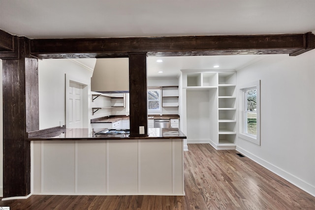 kitchen with beam ceiling, stainless steel dishwasher, wood finished floors, a peninsula, and baseboards