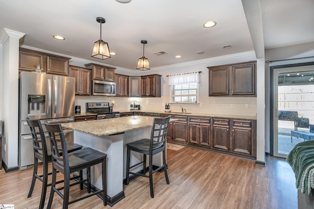 kitchen with a kitchen island, visible vents, appliances with stainless steel finishes, backsplash, and decorative light fixtures