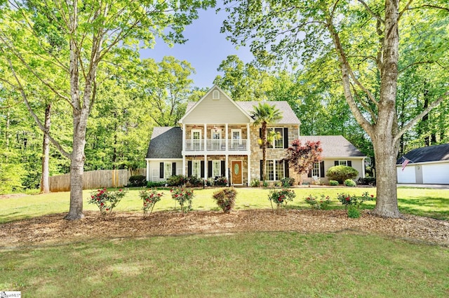 view of front facade with a balcony, stone siding, fence, and a front yard