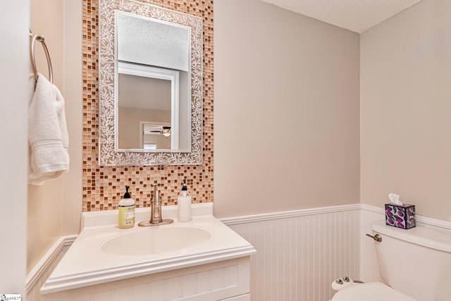 half bathroom featuring a textured ceiling, wainscoting, vanity, and toilet