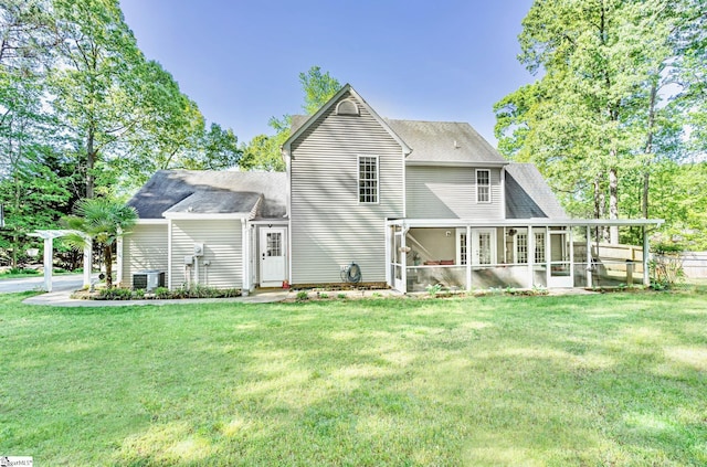 rear view of property featuring a sunroom, roof with shingles, a lawn, and central AC unit