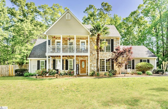 view of front of house featuring a balcony, stone siding, and a front lawn