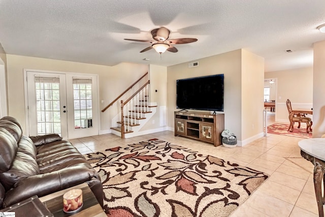 living area featuring light tile patterned flooring, visible vents, a textured ceiling, and stairs