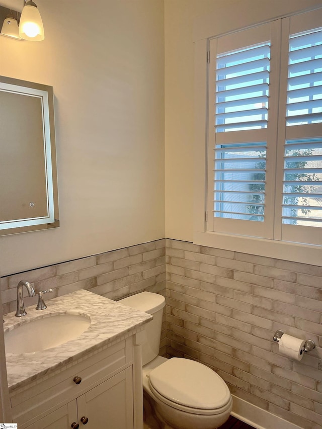 half bath with a wainscoted wall, vanity, toilet, and tile walls