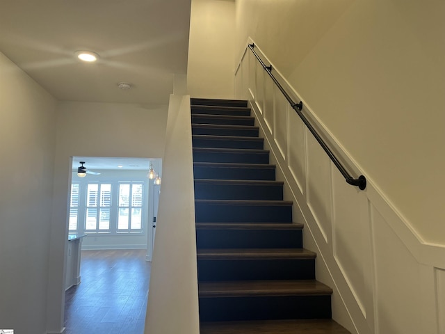 staircase featuring wood finished floors, a ceiling fan, and baseboards