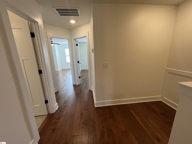 hall with dark wood-type flooring, visible vents, and baseboards