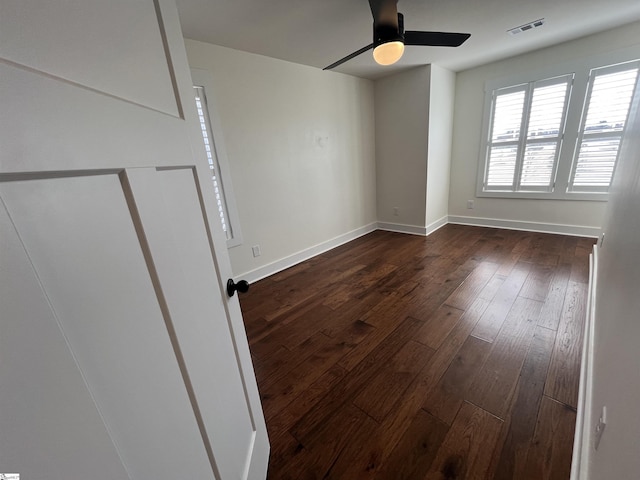 empty room featuring ceiling fan, dark wood-type flooring, visible vents, and baseboards