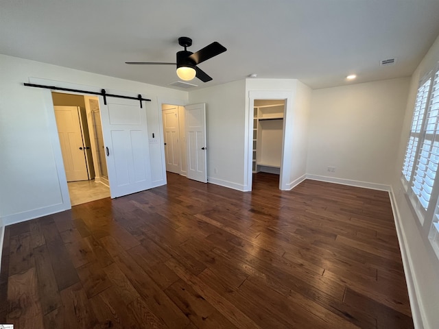 unfurnished bedroom featuring baseboards, a barn door, visible vents, and dark wood-style flooring