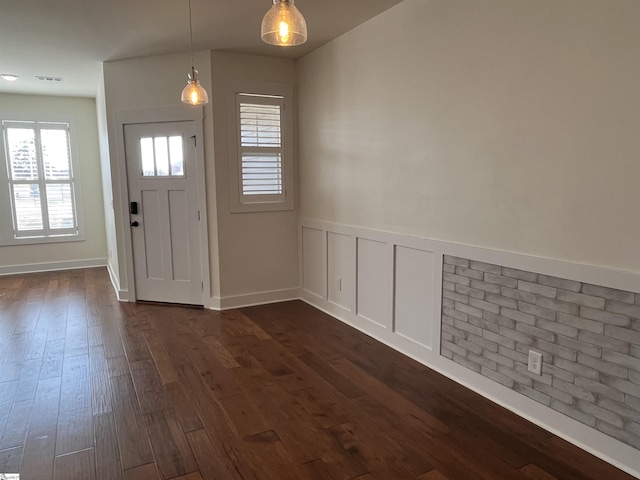 entrance foyer featuring dark wood-style floors, wainscoting, visible vents, and a decorative wall