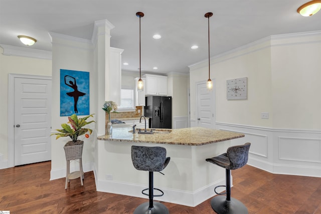 kitchen with a peninsula, light stone countertops, black refrigerator with ice dispenser, white cabinetry, and a sink