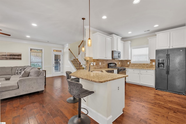 kitchen with a peninsula, a sink, open floor plan, black appliances, and decorative light fixtures