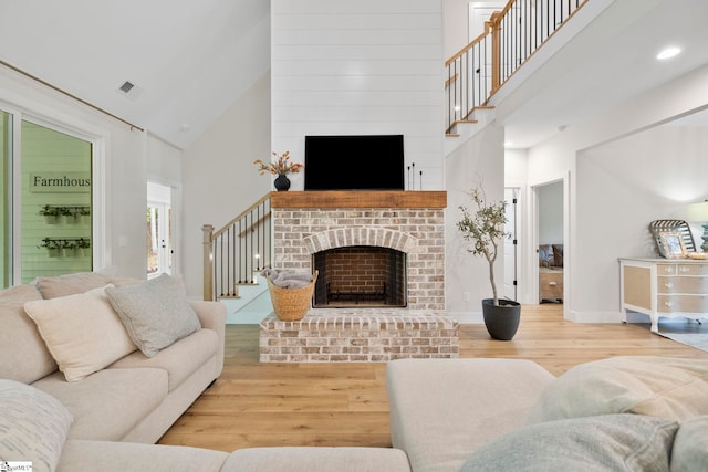 living area featuring light wood-style floors, a fireplace, high vaulted ceiling, and stairway