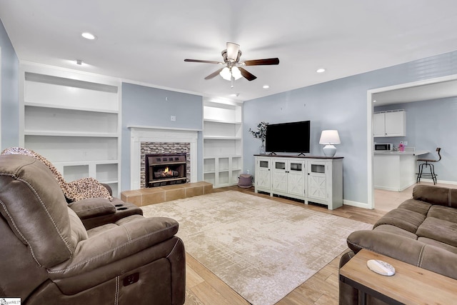 living area with light wood finished floors, a tile fireplace, a ceiling fan, and baseboards