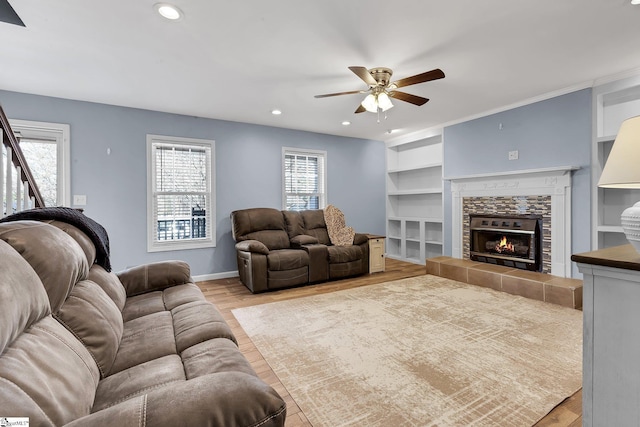 living area featuring built in features, a fireplace, recessed lighting, light wood-style floors, and ceiling fan