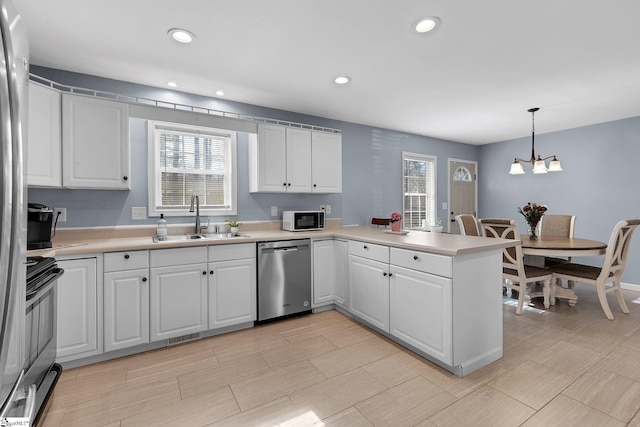 kitchen featuring appliances with stainless steel finishes, decorative light fixtures, a peninsula, light countertops, and white cabinetry