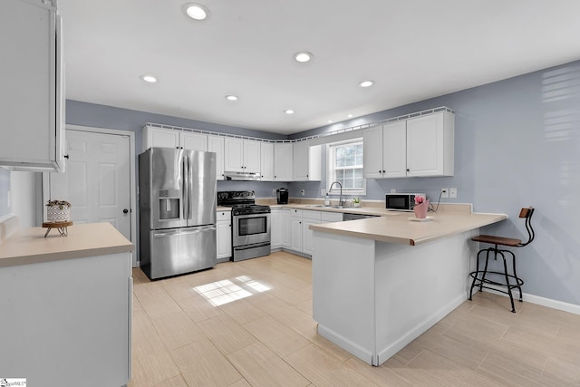 kitchen featuring appliances with stainless steel finishes, a peninsula, light countertops, white cabinetry, and a sink