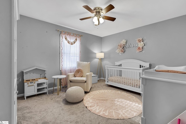 bedroom featuring light colored carpet, ceiling fan, a crib, and baseboards