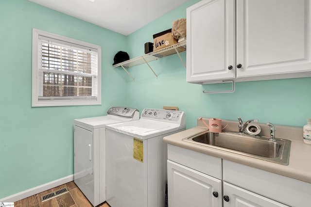 washroom with a sink, visible vents, light wood-type flooring, cabinet space, and washer and clothes dryer