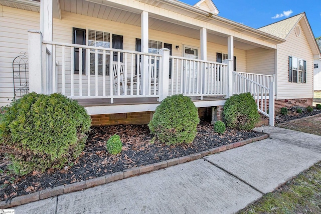 entrance to property with covered porch and a shingled roof