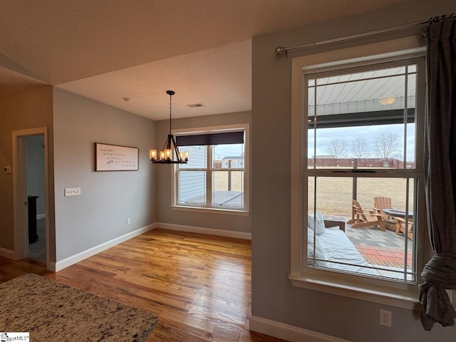 unfurnished dining area with baseboards, light wood-style flooring, visible vents, and a notable chandelier