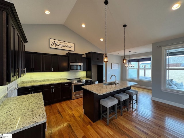 kitchen with a kitchen island with sink, light stone counters, stainless steel appliances, and decorative light fixtures