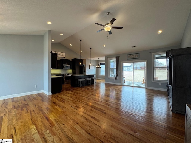 unfurnished living room with lofted ceiling, dark wood-style flooring, baseboards, and a healthy amount of sunlight