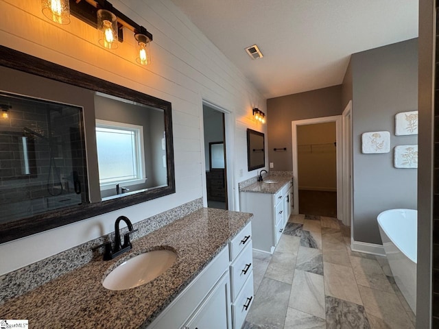 full bathroom with a soaking tub, two vanities, a sink, and a walk in closet