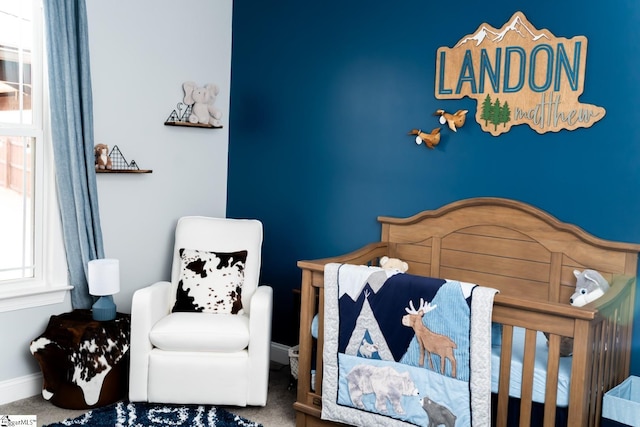 carpeted bedroom featuring a nursery area and baseboards