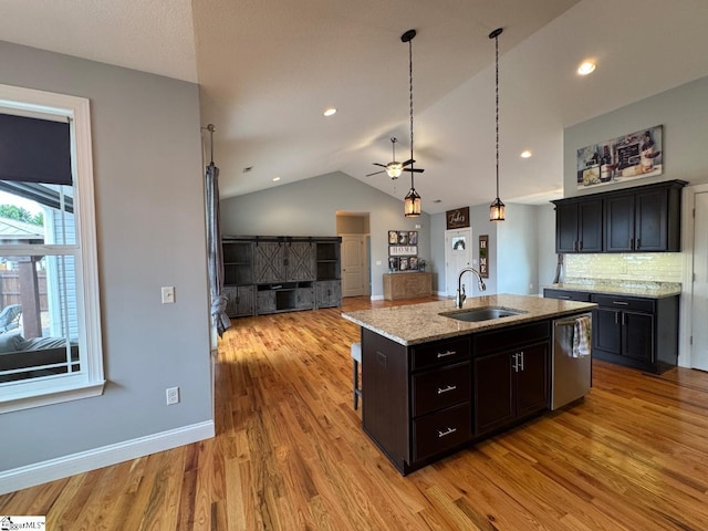 kitchen featuring stainless steel dishwasher, open floor plan, a kitchen island with sink, a sink, and light stone countertops