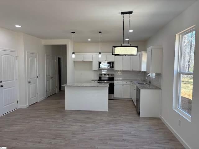 kitchen featuring white cabinets, decorative light fixtures, a center island, stainless steel appliances, and a sink