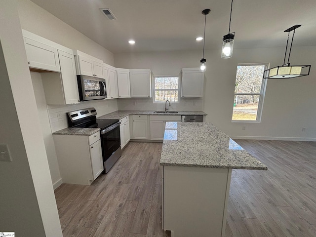 kitchen featuring light stone counters, a center island, decorative light fixtures, stainless steel appliances, and white cabinetry