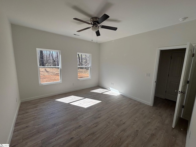 spare room with dark wood-style flooring, a ceiling fan, and baseboards